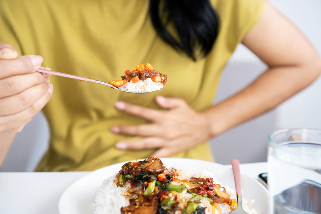 A woman clutches her stomach while eating a plant based meal. if you're new to a plant based diet and are experiencing gas, read our ultimate guide on why plant based diets cause gas and how Shreddies can help.