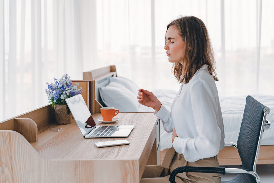 A woman clutches her stomach at work. If you've ever wondered, what is bubble gut, explore our complete guide on what it is and how to get relief.
