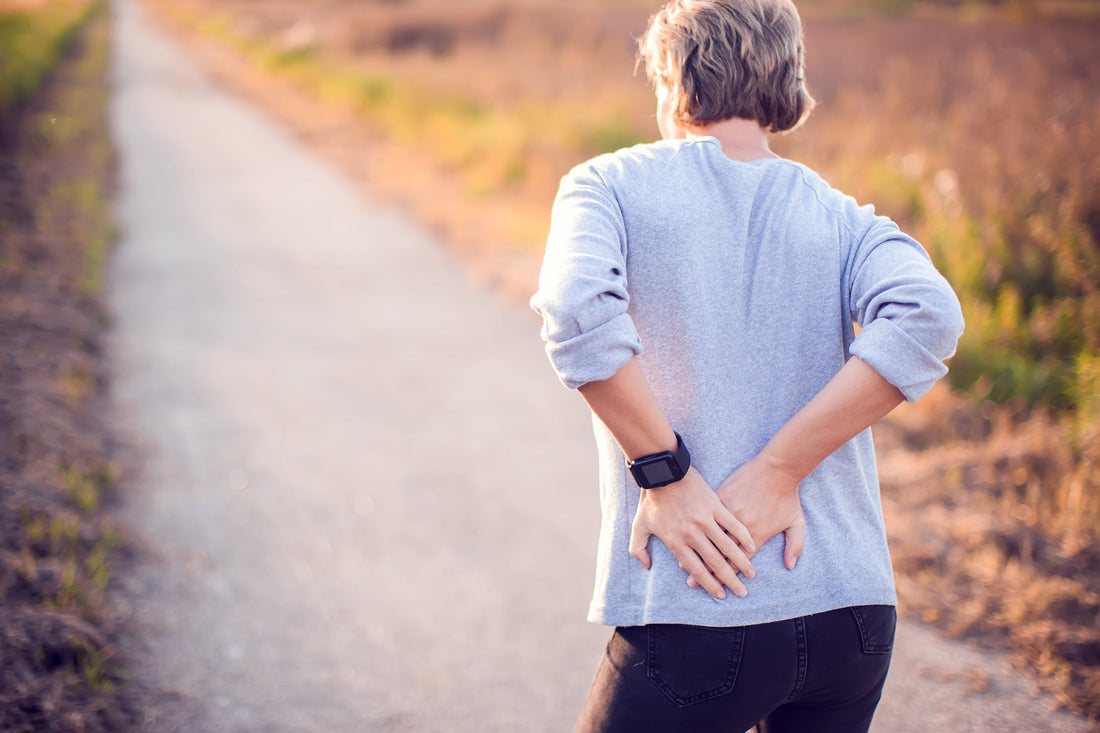 A woman clutches her back. Can gas cause back pain? Learn more in about the gut-spine connection in our complete guide.