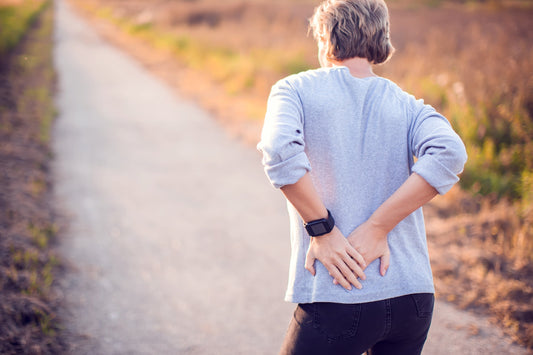 A woman clutches her back. Can gas cause back pain? Learn more in about the gut-spine connection in our complete guide.