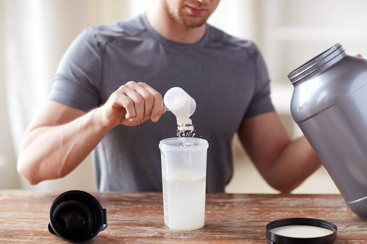 A man adds creatine powder to a water bottle. Does creatine make you gassy? Learn more about the side effects of this common supplement in our complete guide.